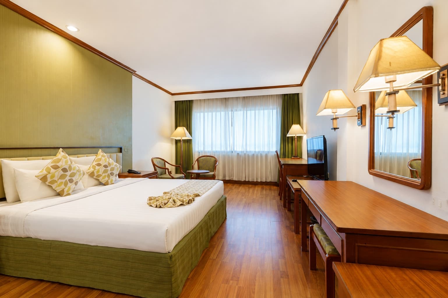 A spacious king room at Arawana Regency Park Sukhumvit, with a green feature wall, desk and city view
