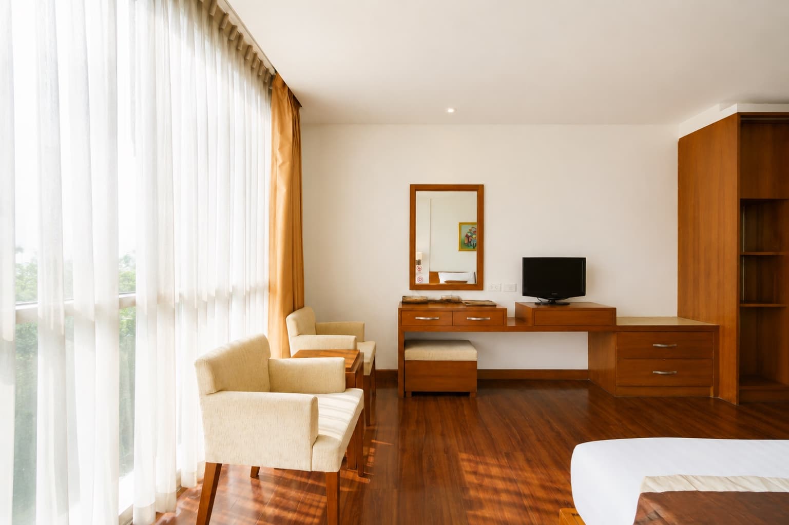 A furnished room with armchairs, a desk and a television beside a bright window at an Arawana property.