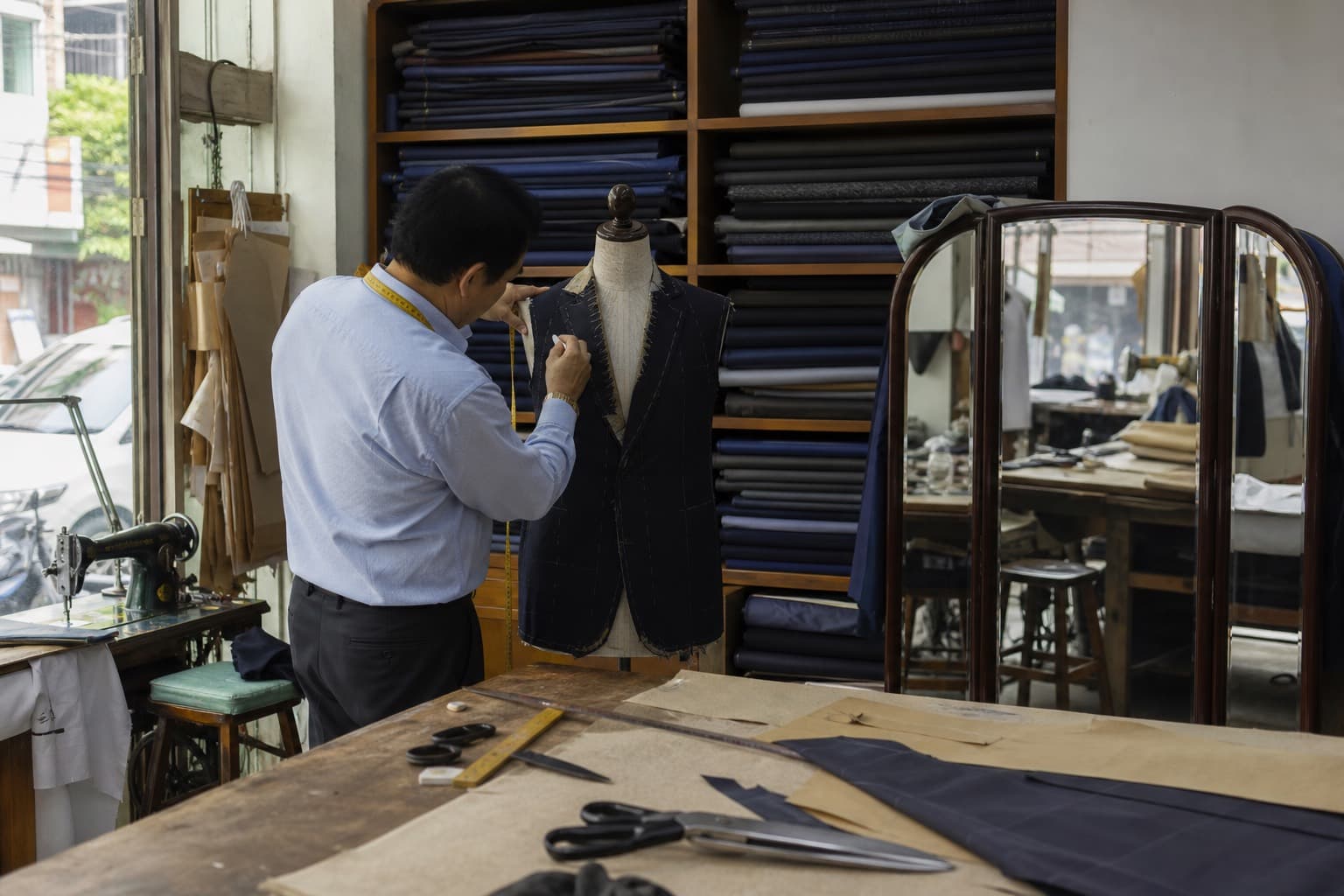 A tailor chalking a half-made jacket on a dress form in a Bangkok workshop