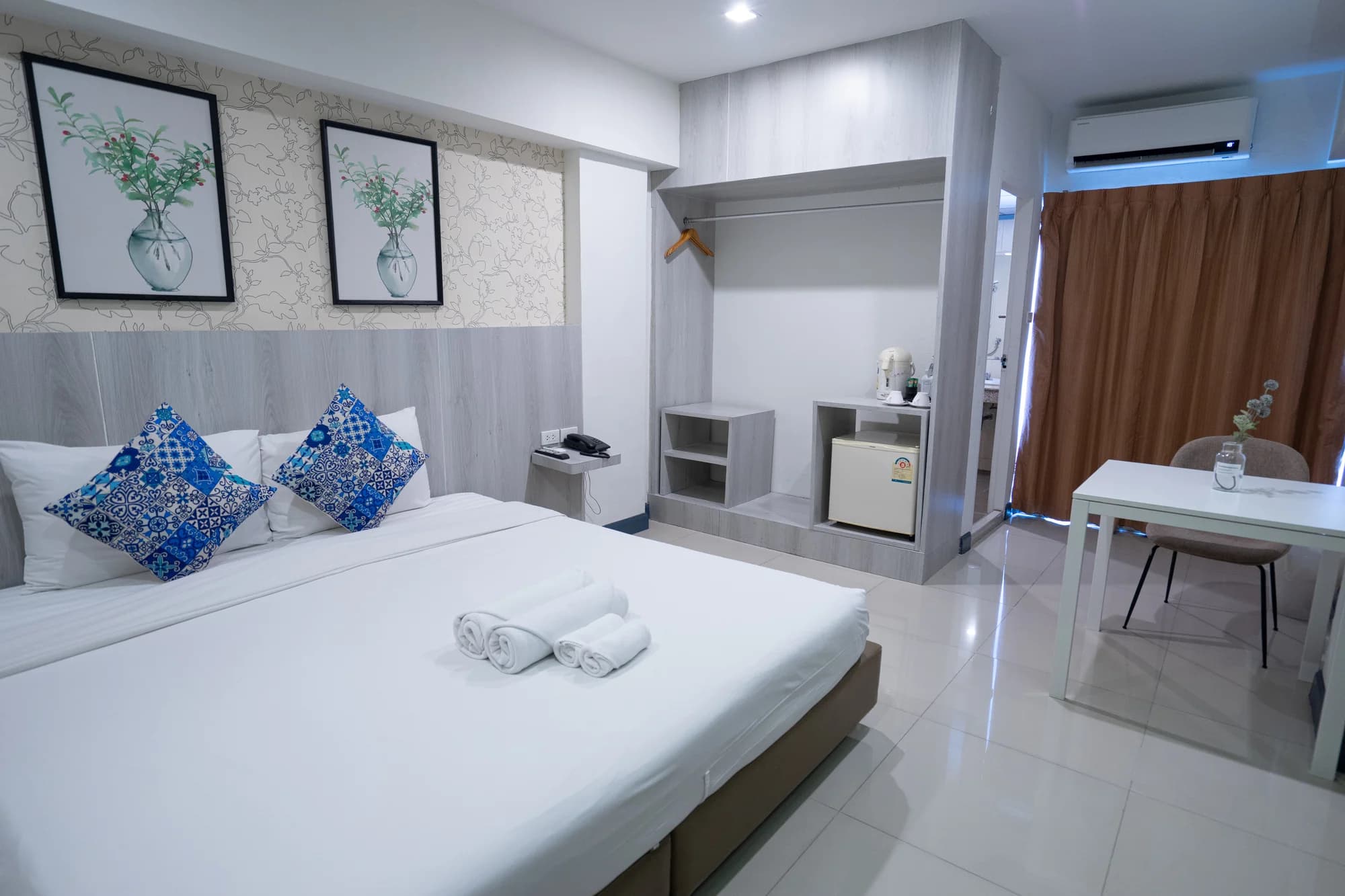 Arawana Regency Srinakarin の Deluxe King Room。キングベッド、青い柄のクッション、窓際のデスク